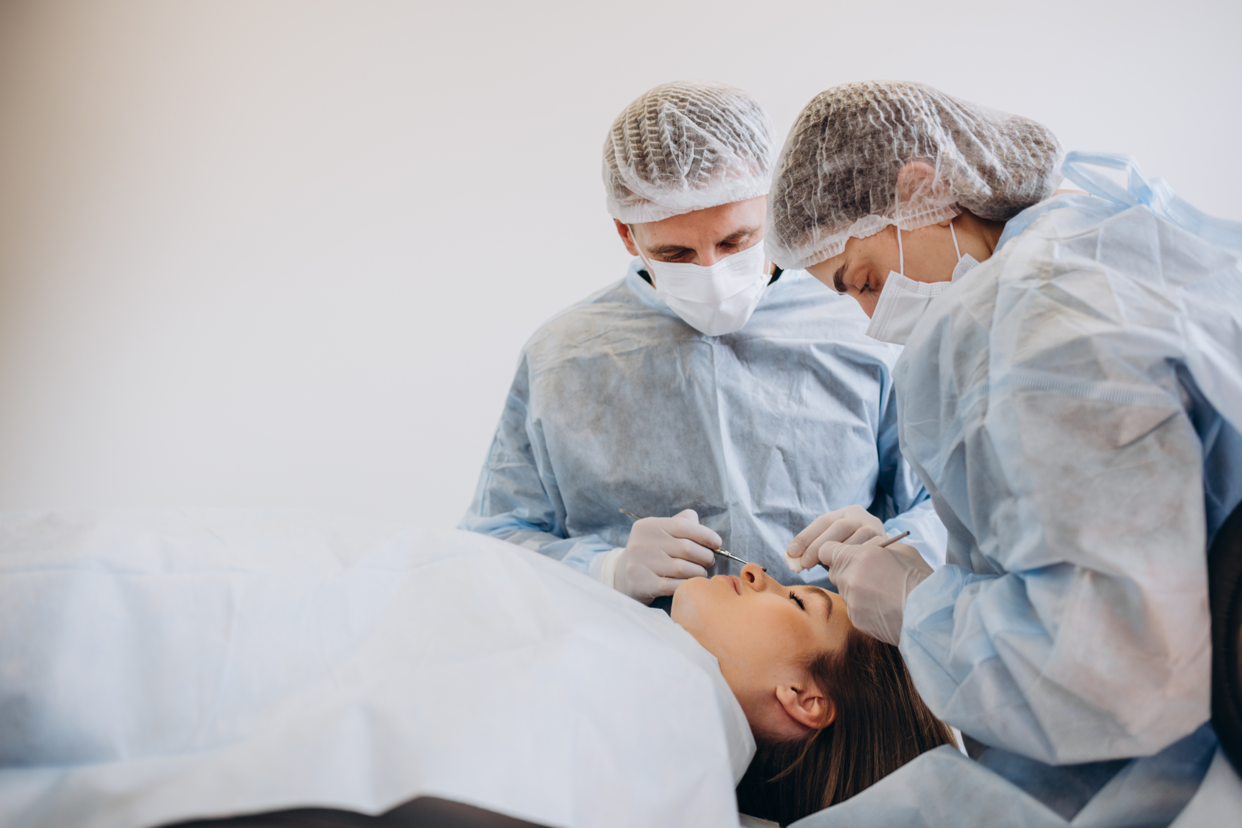 Zwei Chirurgen im Chirurgengewand sehen sich die Nase einer Patientin an