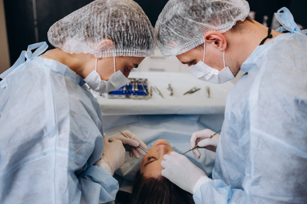 Zwei Chirurgen im Operationsgewand behandeln die Nase einer Patientin, die auf dem Operationstisch liegt