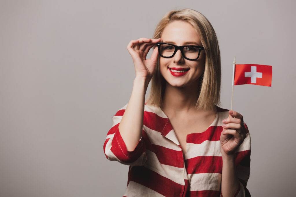 Junge Dame hält die Brille mit einer Hand und die Flagge der Schweiz in der anderen Hand