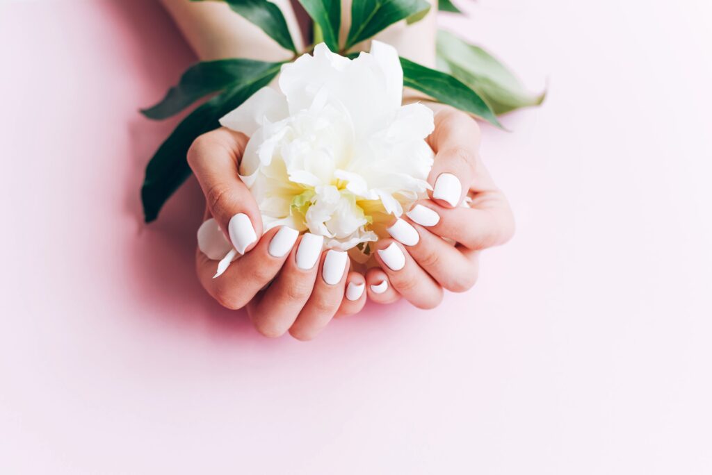 Frau mit weiß lackierten Nägeln hält eine weiße Blume in der Hand