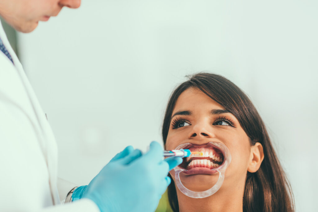 Frau mit geöffnetem Mund wird von einem Zahnarzt behandelt