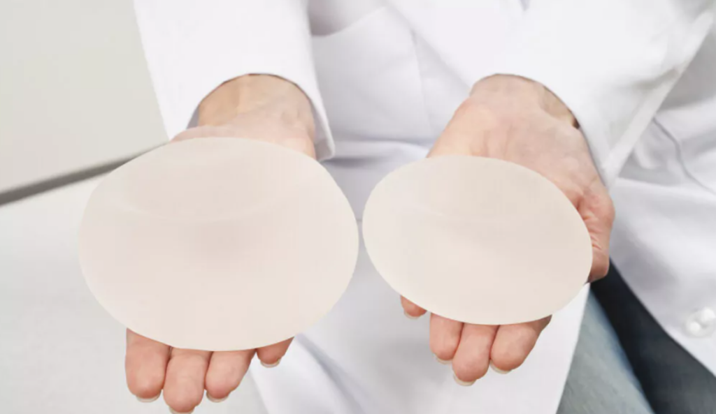 zwei Handflächen auf denen zwei Brustimplantate liegen