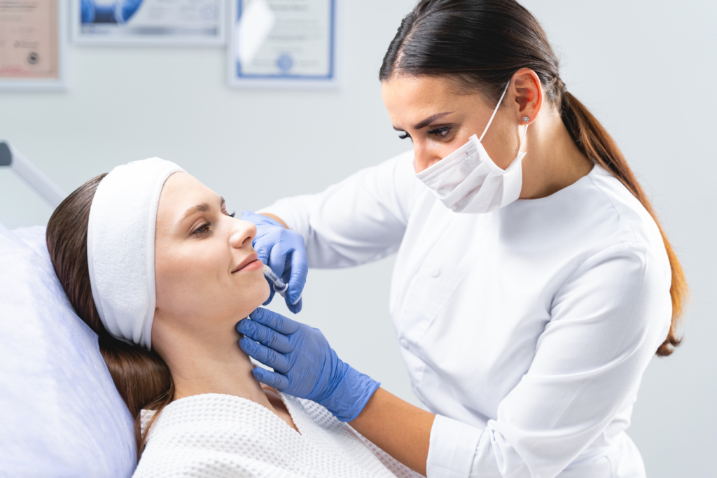 Frau im Arztgewand spritzt Patientin etwas in die Gesichtshaut