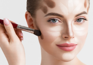 Junge Frau die geschminkt wird. Ein Hand hat einen Pinsel und streicht damit über das Gesicht der Frau