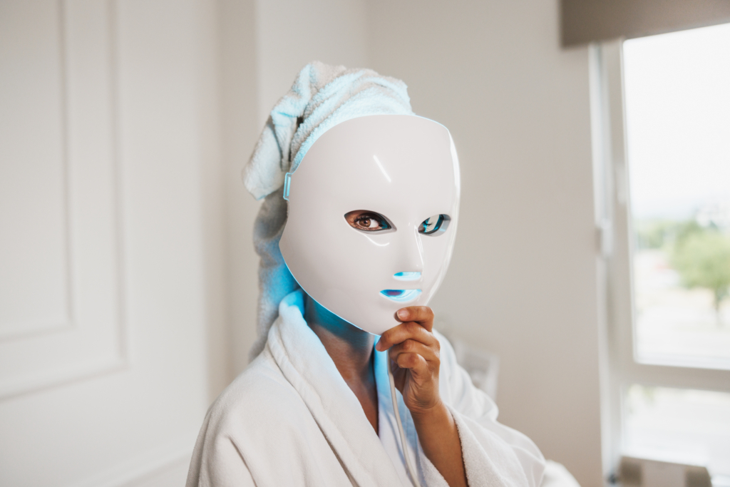 Frau hält sich blaue LED-Maske vor das Gesicht.