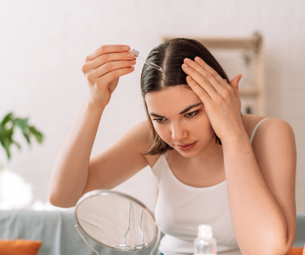 Frau sitzt vor einem Kosmetikspiegel und gibt sich Haaröl in die Haare