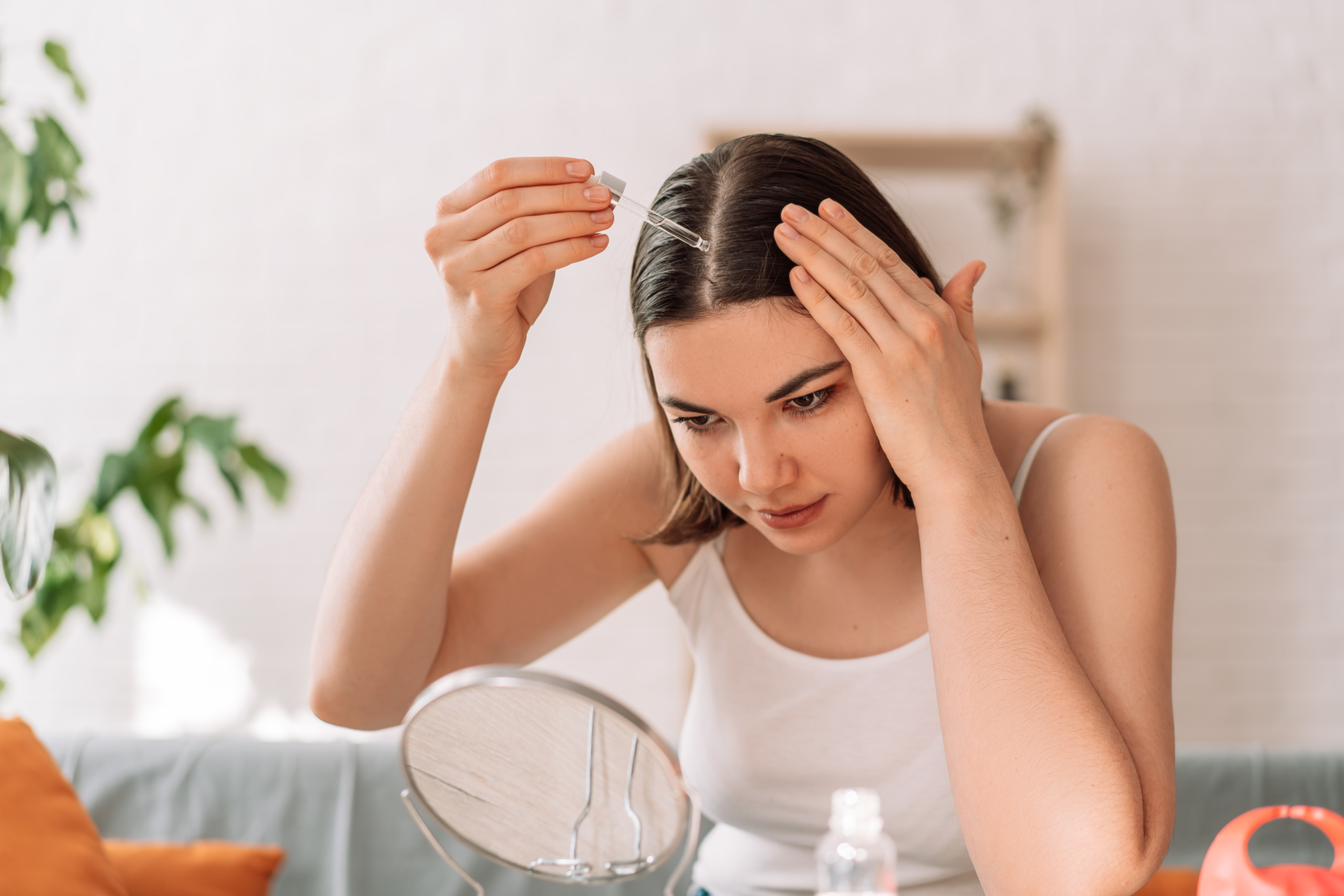 Frau sitzt vor einem Kosmetikspiegel und gibt sich Haaröl in die Haare