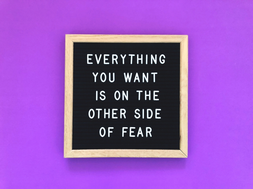 Schild mit Everythin you want is on the other side of fear auf einem lila Hintergrund