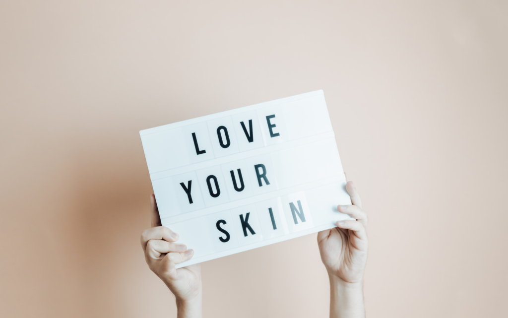 Schild mit Love your Skin das von zwei Händen gehoben wird