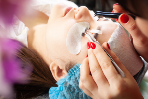 Frauengesicht mit Pads und eine Frau die die Wimpern behandelt