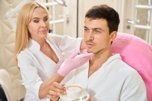 Mann auf einer Kosmetikliege hält einen Kaffee in der Hand. eine Frau hält sein Gesicht