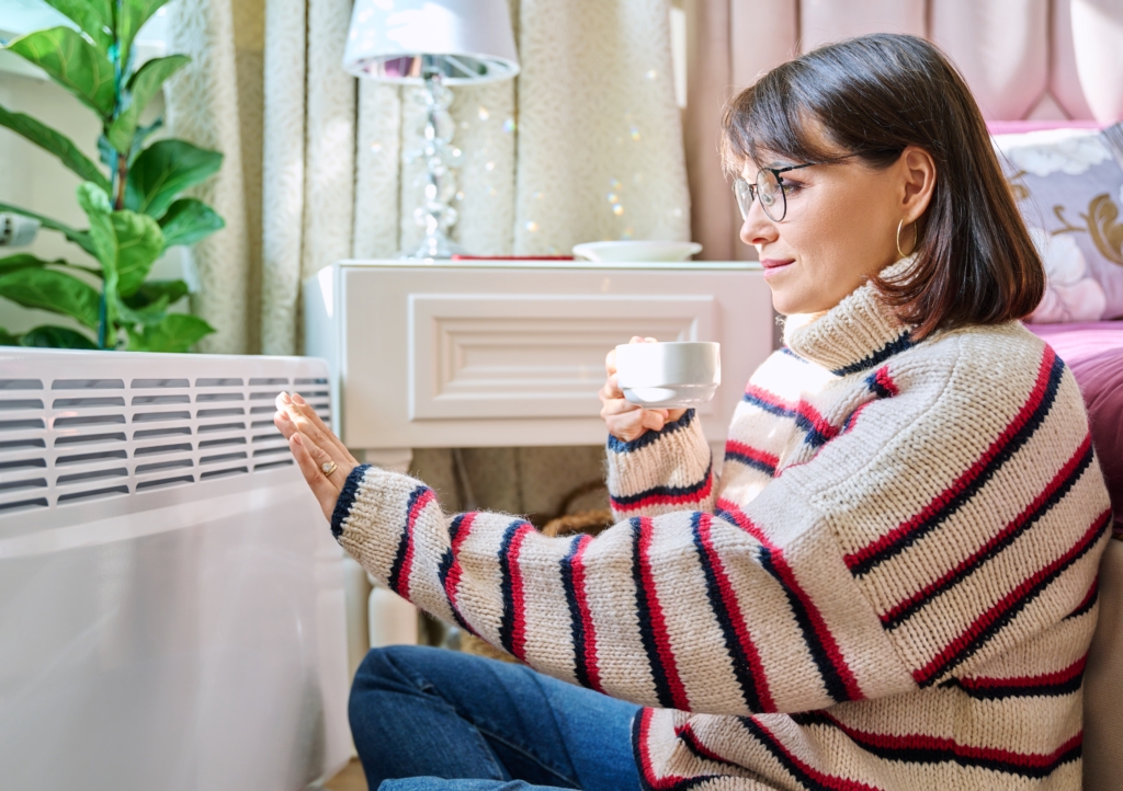 Frau sitzt vor Heizkörper
