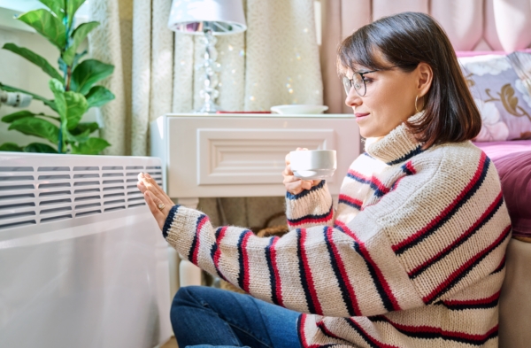Frau sitzt vor Heizkörper