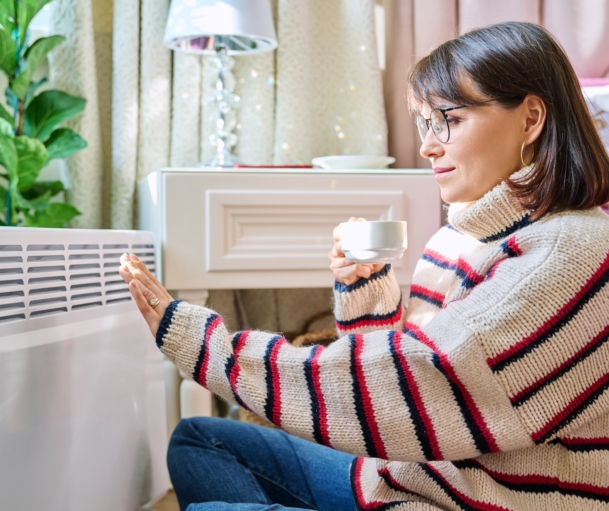 Frau sitzt vor Heizkörper